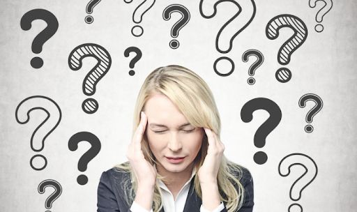 Woman in a blazer presses her temples with eyes closed among drawn question marks.
