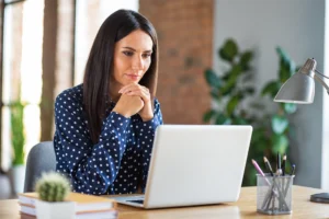 Woman working on a laptop at a desk in a bright, sunlit home office