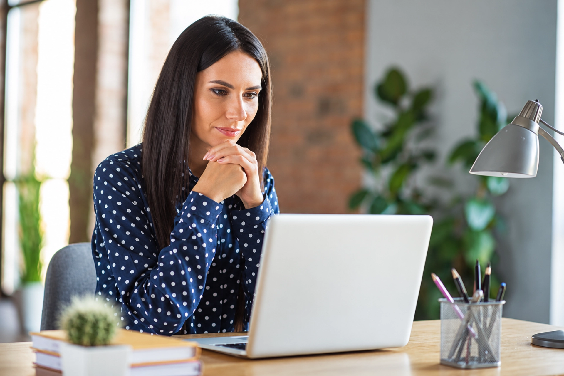 Woman working on a laptop at a desk in a bright, sunlit home office