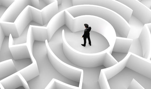 Man in a dark suit stands in the center of a large white circular maze.