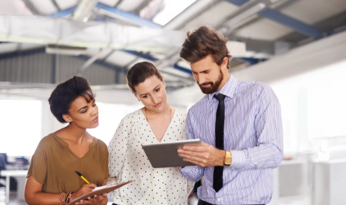 A man with a tie holding a tablet while reviewing notes with two female colleagues.
