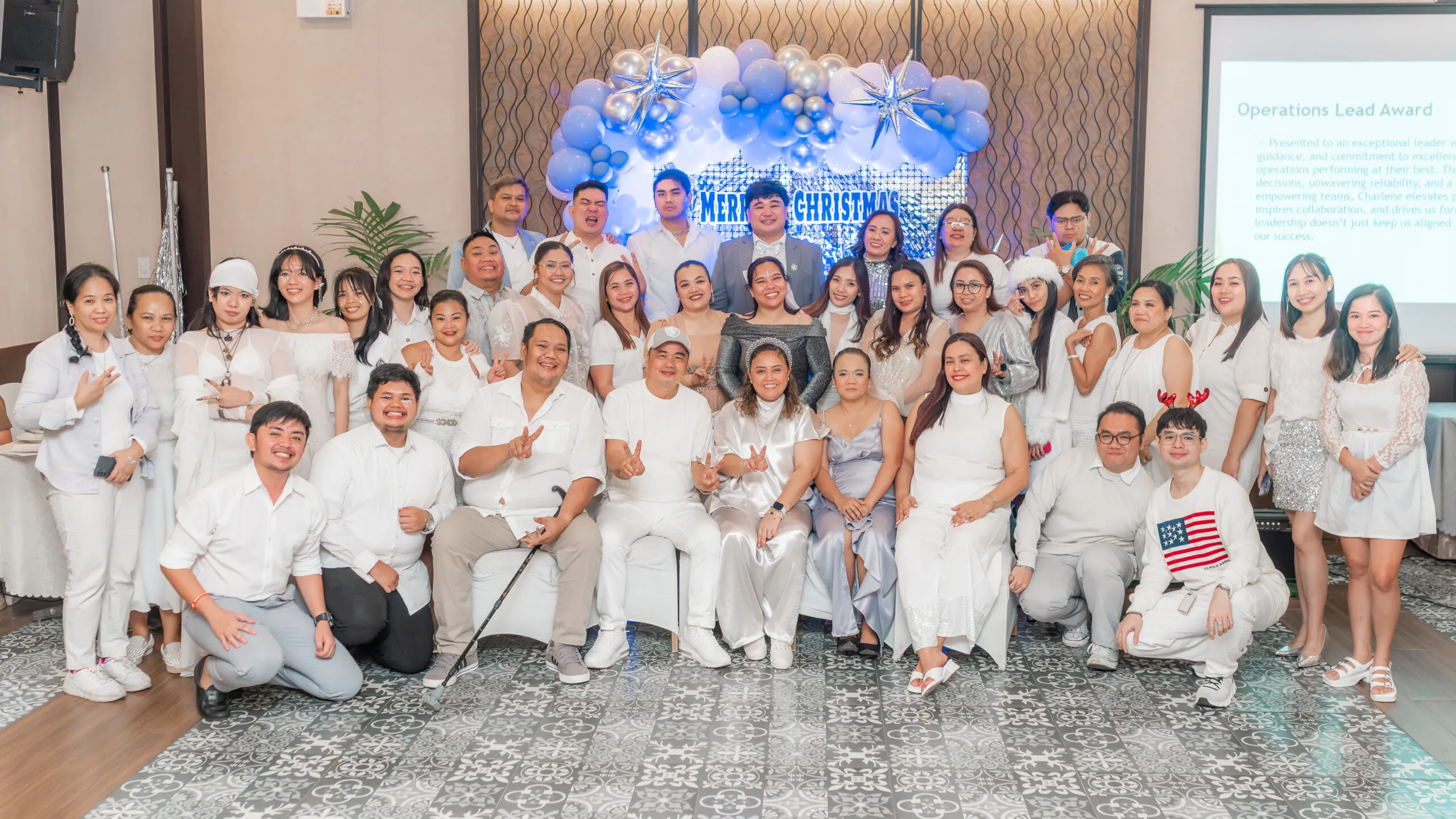 A large group of Virtual360 colleagues dressed in white outfits posing in front of a Christmas balloon display.
